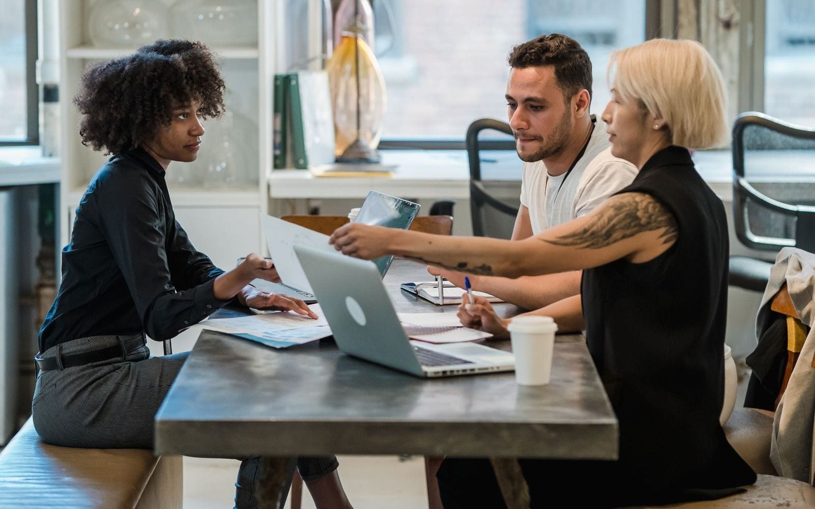 Three colleagues around a meeting table reviewing printed documents and a laptop
